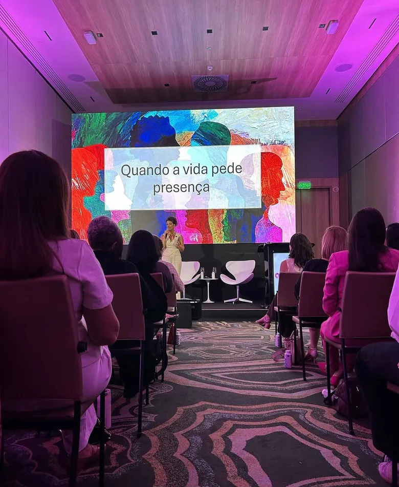 Plateia acompanhando a palestra de Ediane Ribeiro, com o slide “Quando a vida pede presença” projetado no palco